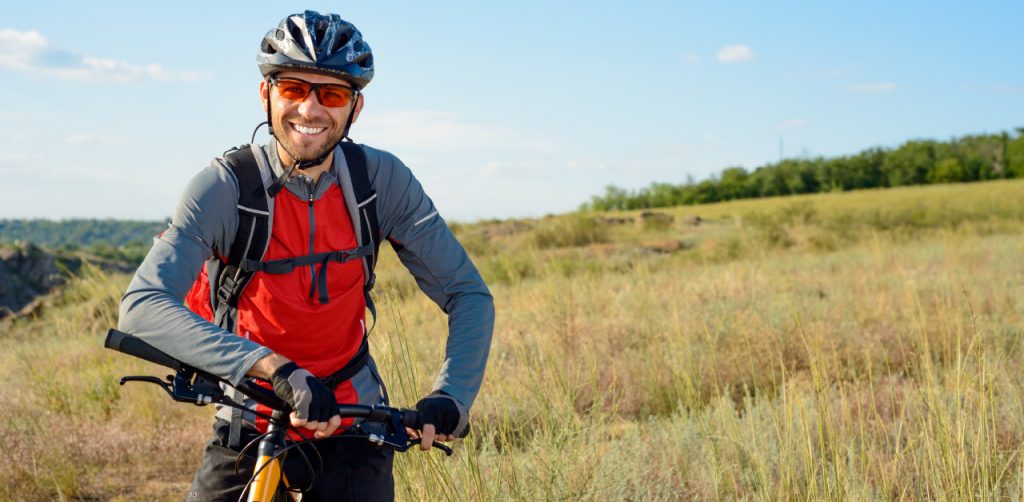 a gentlemen riding a bike outdoors wearing protective eye gear and smiling