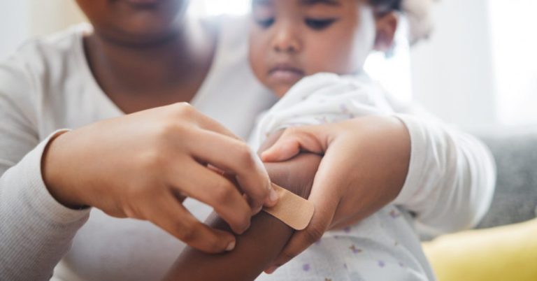 father putting a bandage on his child that has scrapes and cuts