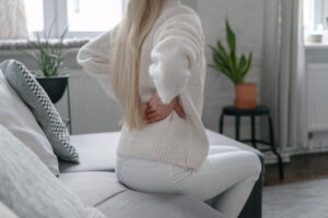 Woman feeling back ache and sitting on couch at home