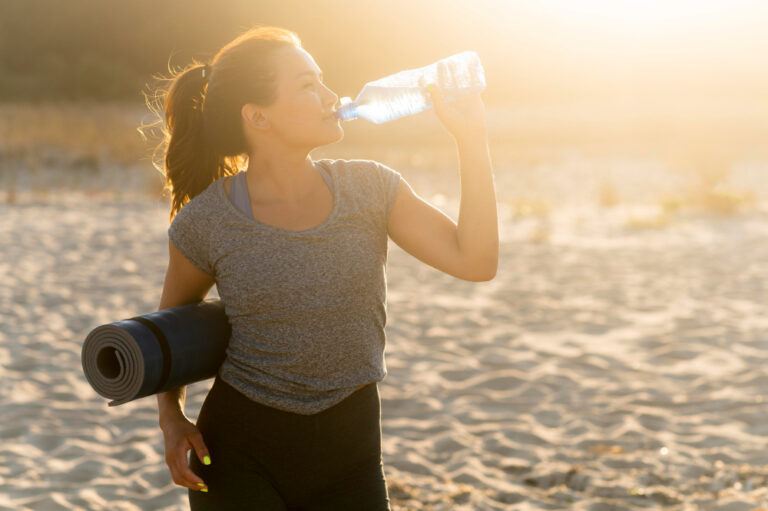 woman at the beach drinking water as part of her hydration goals