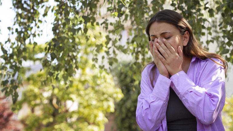 woman sneezing and suffering from common allergy symptoms outside