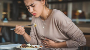 woman in pain holding her stomach from food poisoning while eating a meal at the table