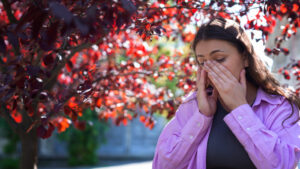 a woman with brown hair wearing a pink jacket suffering from seasonal allergies outisde