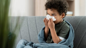 a small child sitting on a couch blowing into a napkin sick during flu season
