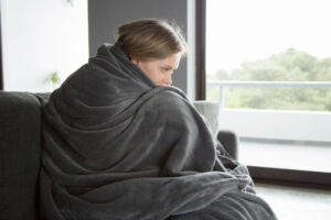 Person wrapped in a blanket sitting on a couch, resting with aches and pains.