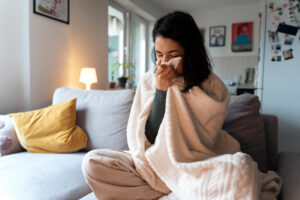 Person wrapped in a blanket sneezing on a couch, highlighting concerns about indoor air quality.